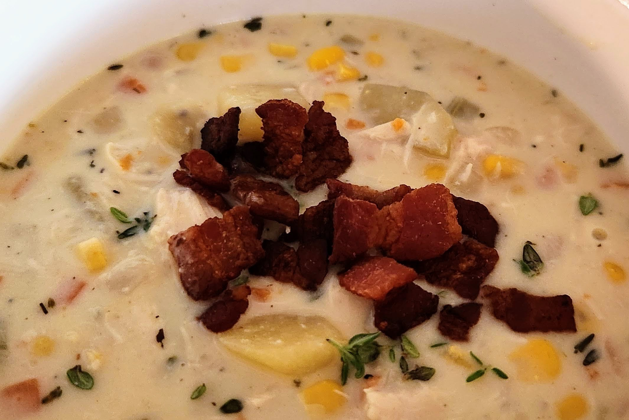 Bowl of chicken corn chowder garnished with bacon crumbles and fresh thyme